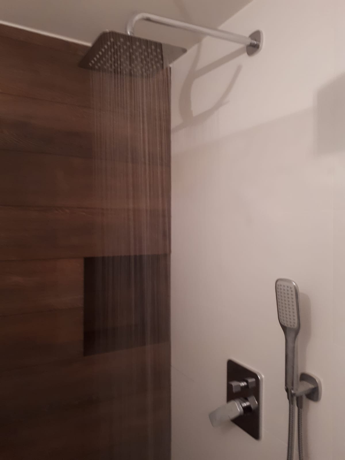 Nowoczesna kabina prysznicowa z deszczownicą i panelem z ciemnego drewna, strumień wody w trakcie użytkowania, widoczna bateria termostatyczna i słuchawka prysznicowa.