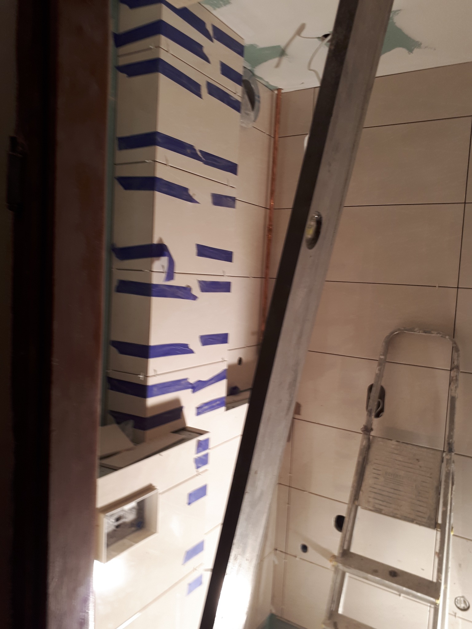 W trakcie zabudowy pionu wentylacyjnego płytami kartonowo-gipsowymi w łazience, zabezpieczonymi taśmą malarską, widoczna poziomica i drabina.