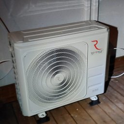 Eko-KlimaWent Bobowicz - Biała, zewnętrzna jednostka klimatyzacji Rotenso Hiro, umieszczona na drewnianej podłodze przy ścianie z oknem. Widoczne przewody i logo producenta.