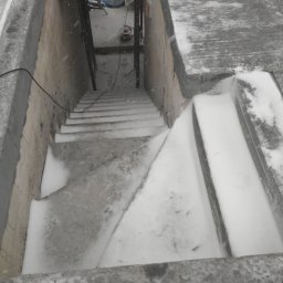Ingbau Spólka z Ograniczoną Odpowiedzialnością Sp. z o.o - Surowe betonowe schody w dół, częściowo pokryte śniegiem, widoczne narzędzia budowlane i drabina w tle.