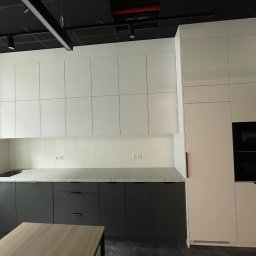 Netkam Anna Suszka - Nowoczesna kuchnia z szarymi szafkami dolnymi, jasnym blatem i białymi szafkami górnymi, zabudowana z piekarnikiem i mikrofalówką, oświetlenie punktowe na czarnym suficie.