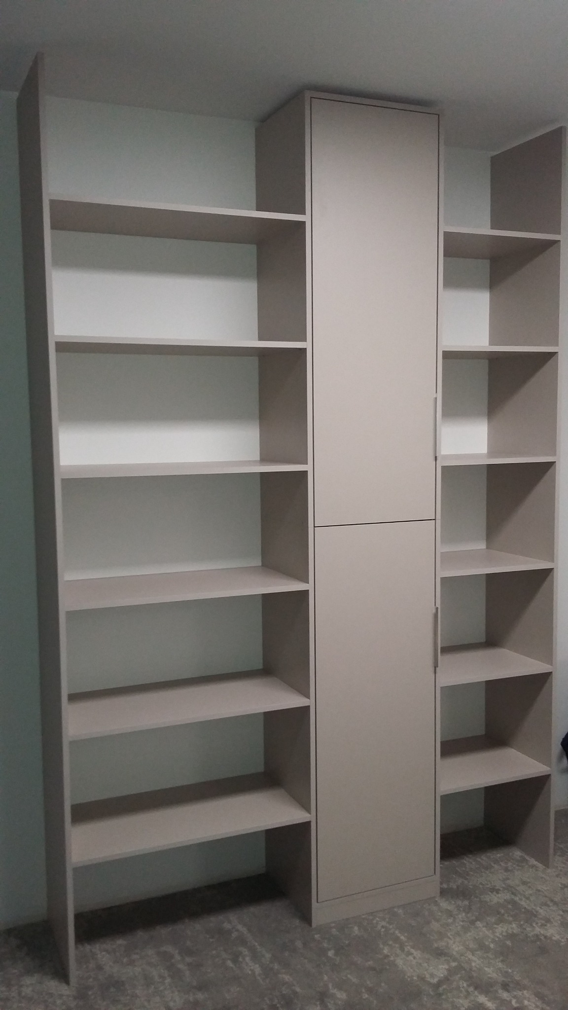 Beżowy regał z szafką pośrodku, widok od dołu, puste półki, szara podłoga.