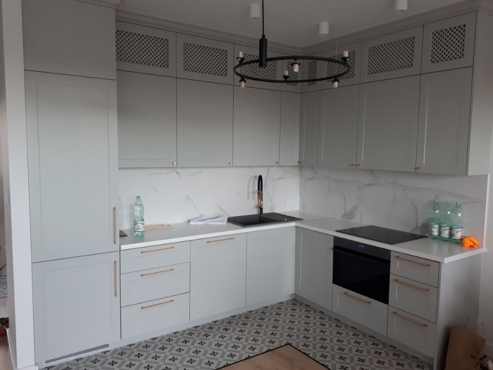 Jasnoszara kuchnia z białym blatem i marmurowym backsplashiem, wzorzysta podłoga, nowoczesne oświetlenie sufitowe.