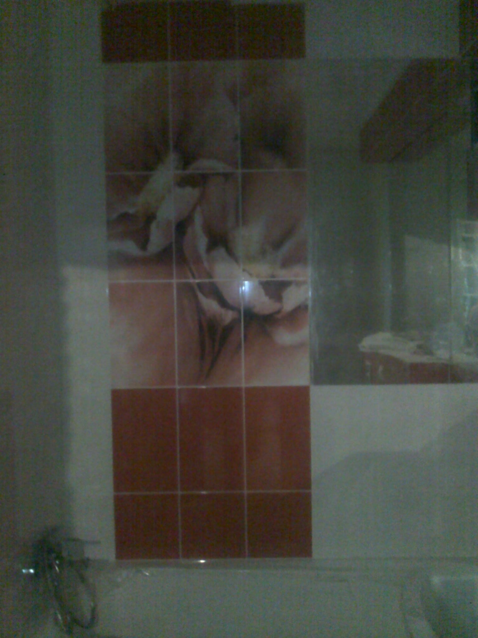 Fragment ściany w łazience z brązowymi i beżowymi płytkami z motywem kwiatowym, widoczne narzędzia w dolnym lewym rogu.