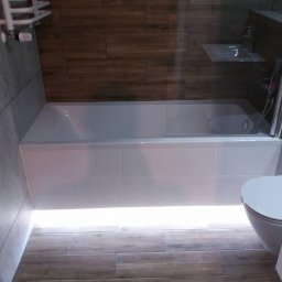 NK Norbert Kudła - Wykończona łazienka z podświetlaną wanną, drewnopodobnymi płytkami podłogowymi i ściennymi oraz grzejnikiem drabinkowym.