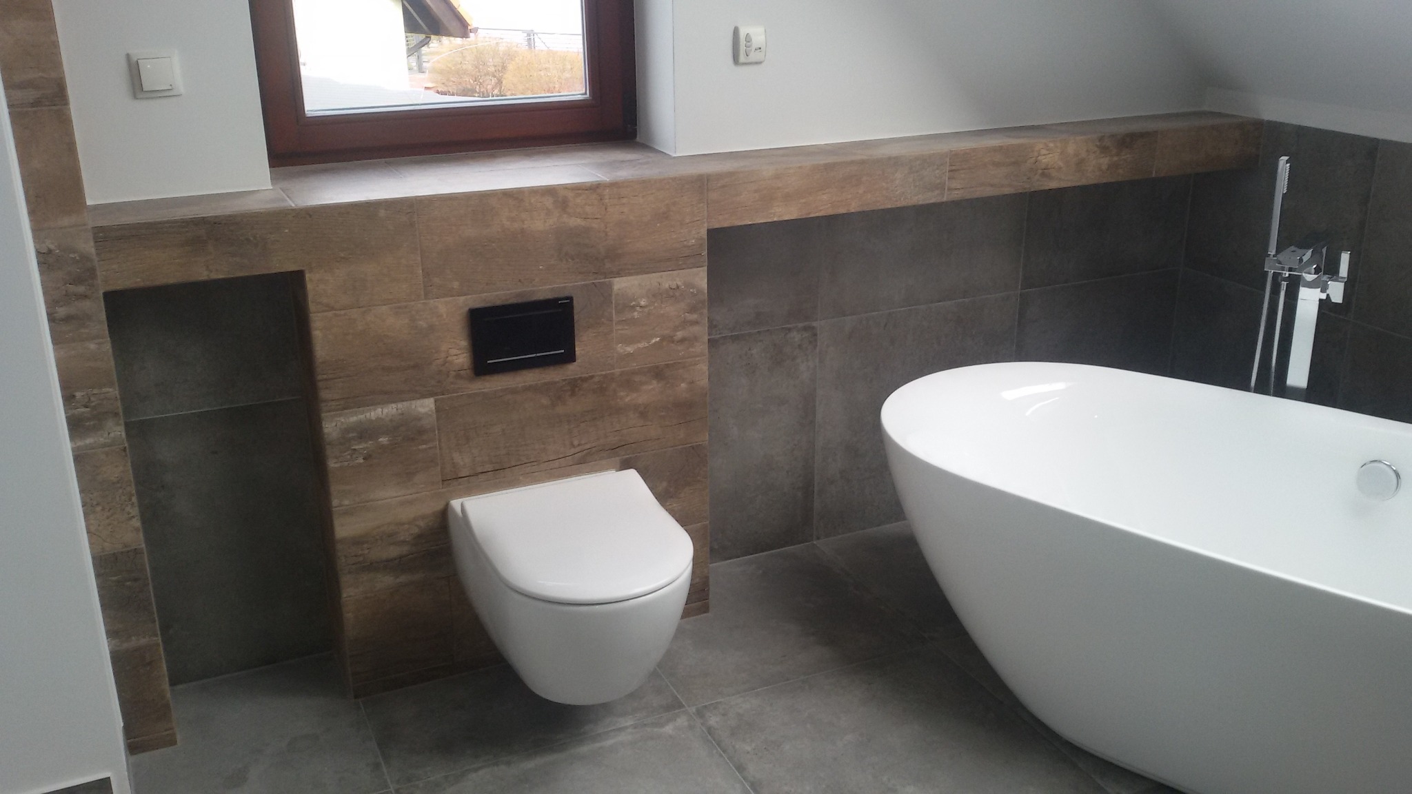 Nowoczesna łazienka z wolnostojącą wanną, podwieszaną miską WC i płytkami imitującymi drewno na ścianach.