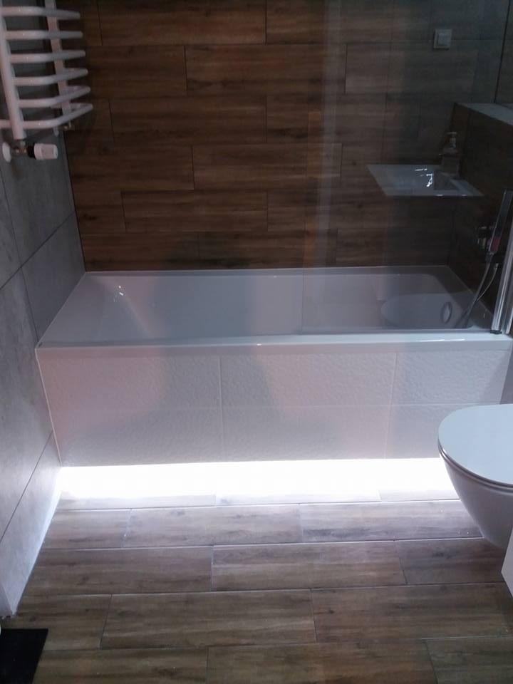 Wykończona łazienka z podświetlaną wanną, drewnopodobnymi płytkami podłogowymi i ściennymi oraz grzejnikiem drabinkowym.