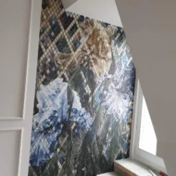 Ściana pokryta mozaiką z motywem kwiatowym, irysy w odcieniach niebieskiego i brązu, widok z dołu schodów, fragment białych drzwi po lewej stronie.