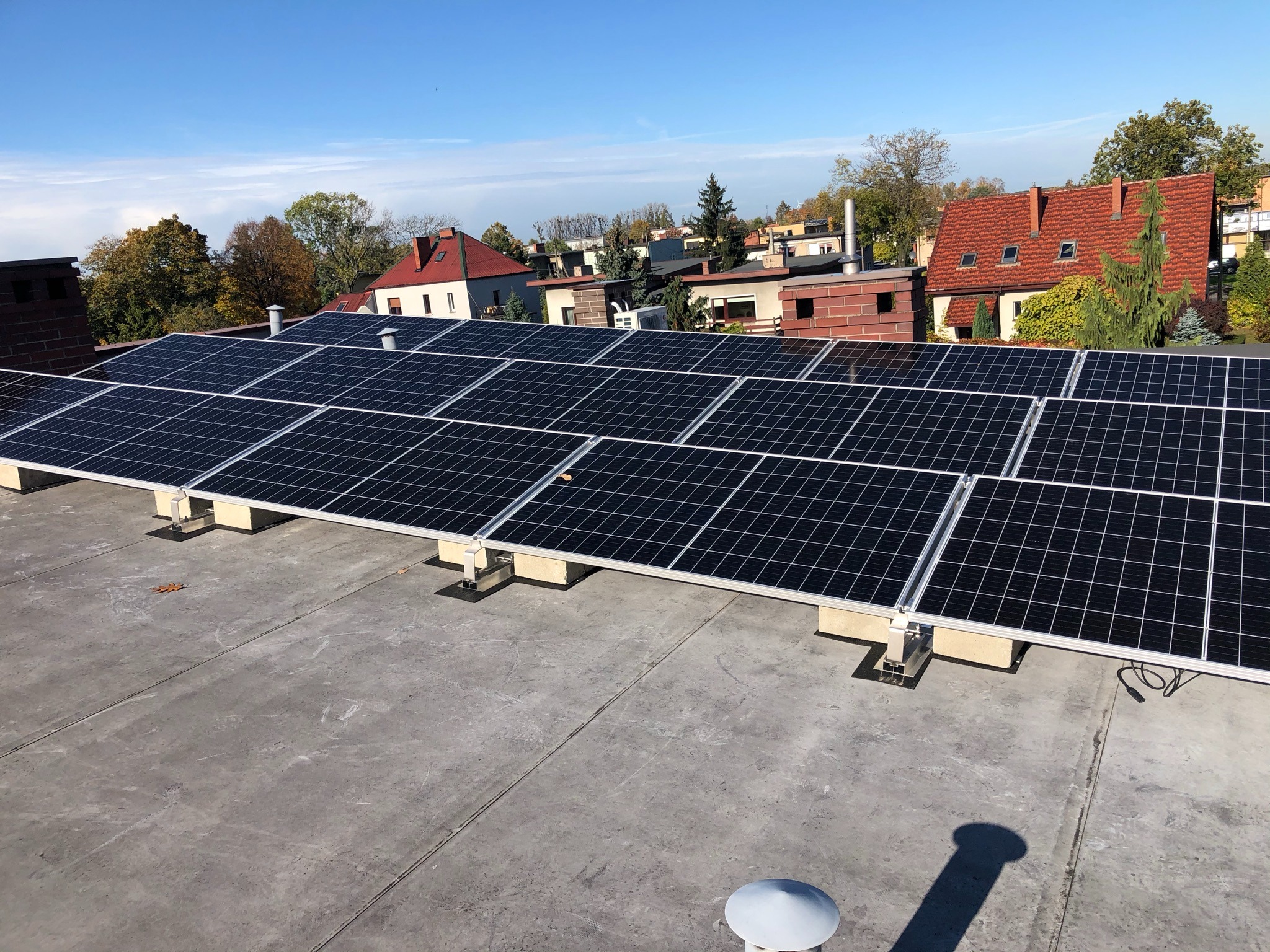 Czarny panel słoneczny na szarym dachu z widokiem na osiedle domów jednorodzinnych w słoneczny dzień.