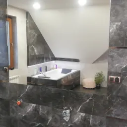 Nowoczesna łazienka z czarnymi marmurowymi płytkami z miedzianymi akcentami, widoczna wanna pod skosem dachu, oświetlenie LED i dekoracyjne dodatki.