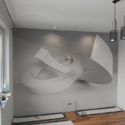 Pokój w trakcie prac wykończeniowych: panele podłogowe częściowo ułożone, na ścianie fototapeta z motywem abstrakcyjnym, widoczne narzędzia i chemia gospodarcza na parapecie okna.