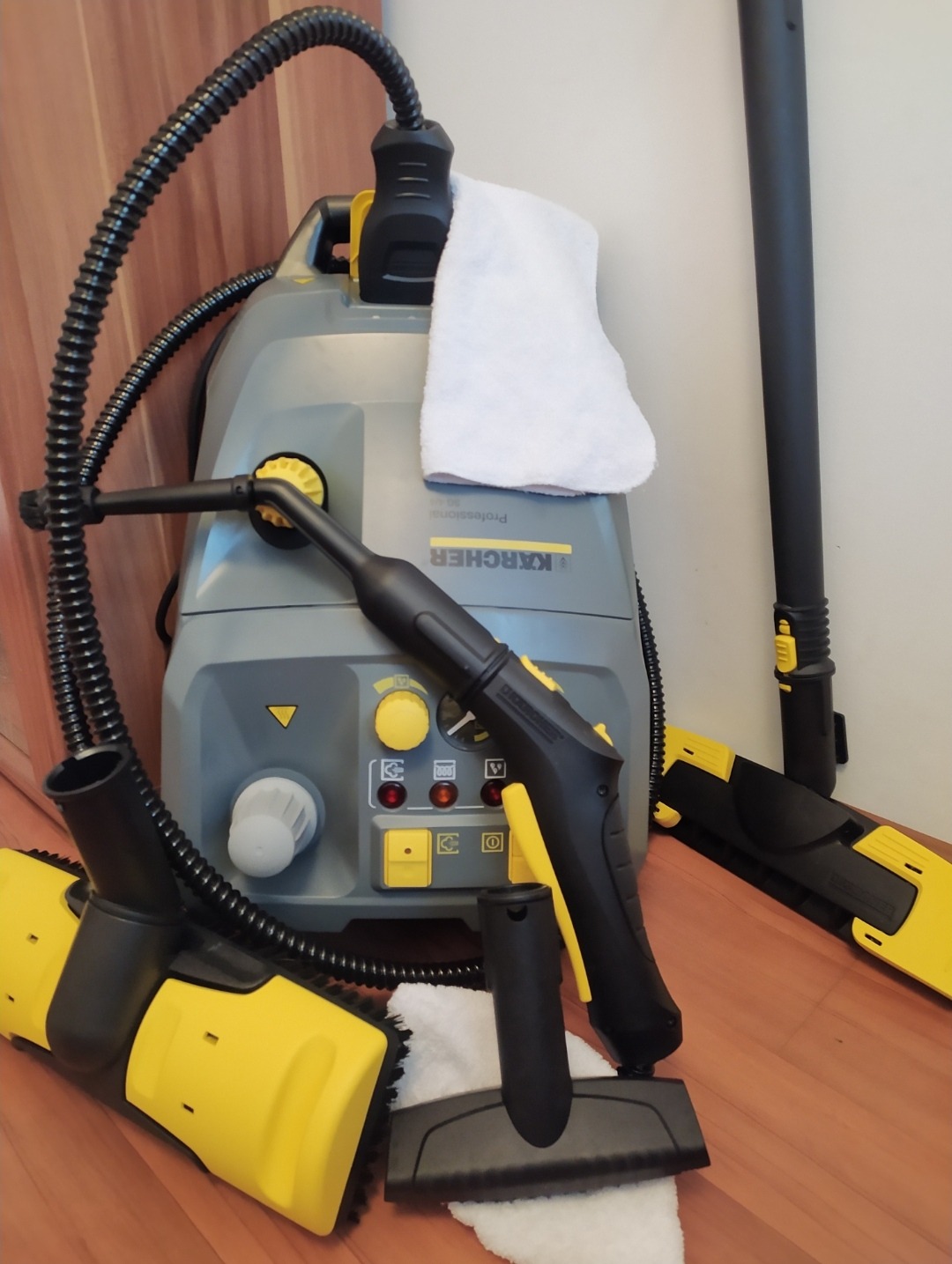 Profesjonalny parowy odkurzacz Karcher z akcesoriami do czyszczenia tapicerki i dywanów, widoczne różne końcówki i ściereczki na drewnianej podłodze.
