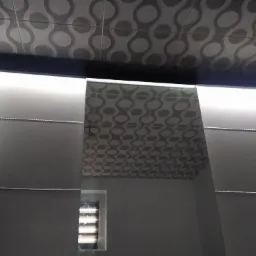 Nowoczesna łazienka z podświetlanym sufitem i lustrami, widoczne geometryczne płytki sufitowe i fragment okna z żaluzjami.