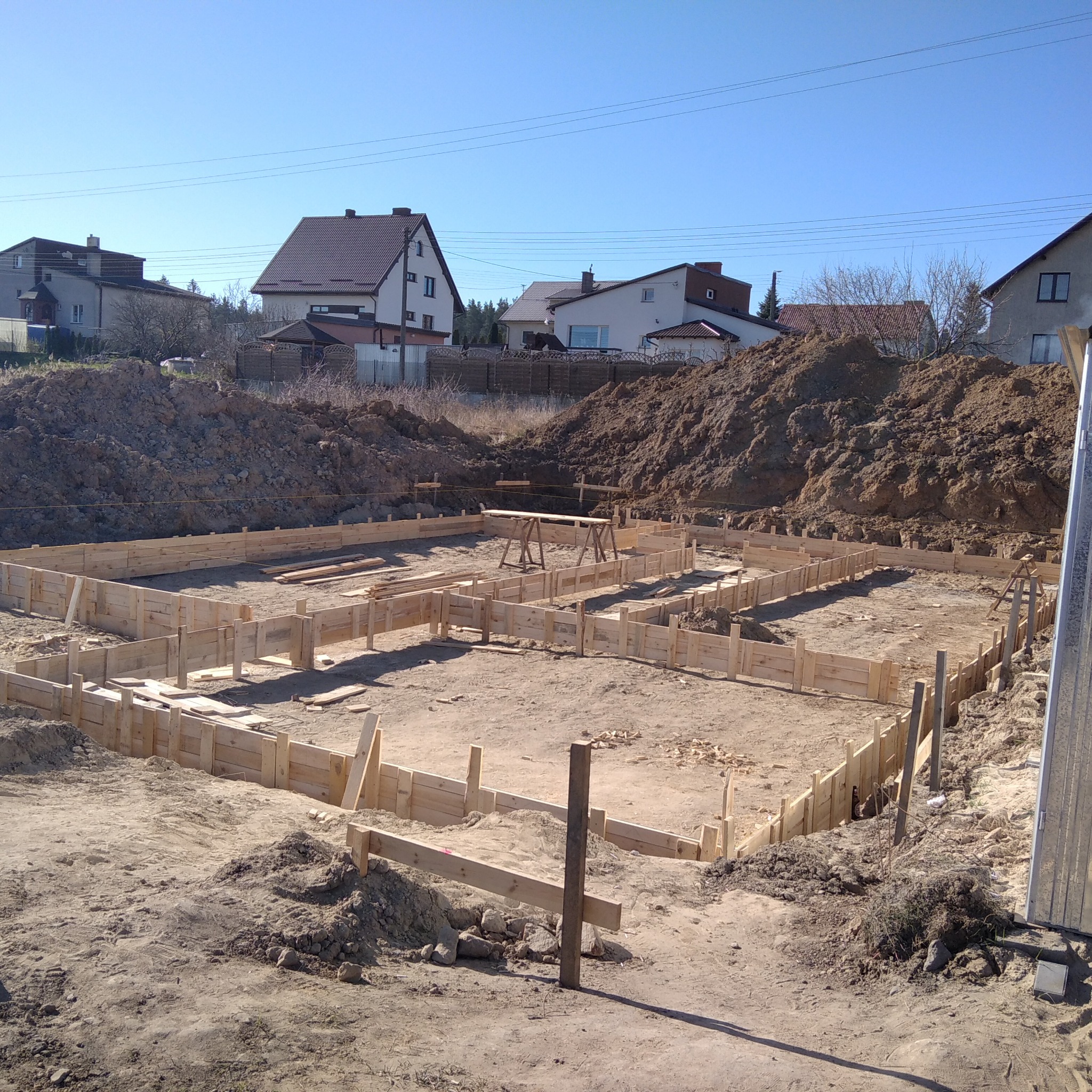 Wykonanie drewnianego szalunku pod fundamenty domu jednorodzinnego na działce, widoczne elementy konstrukcyjne i wykop pod budynek.