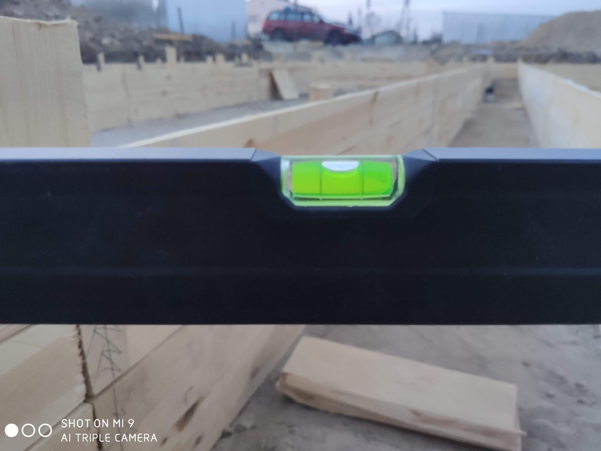 Poziomica na tle drewnianego szalunku fundamentów w Starogardzie Gdańskim, widoczny wykop i fragment samochodu w tle.