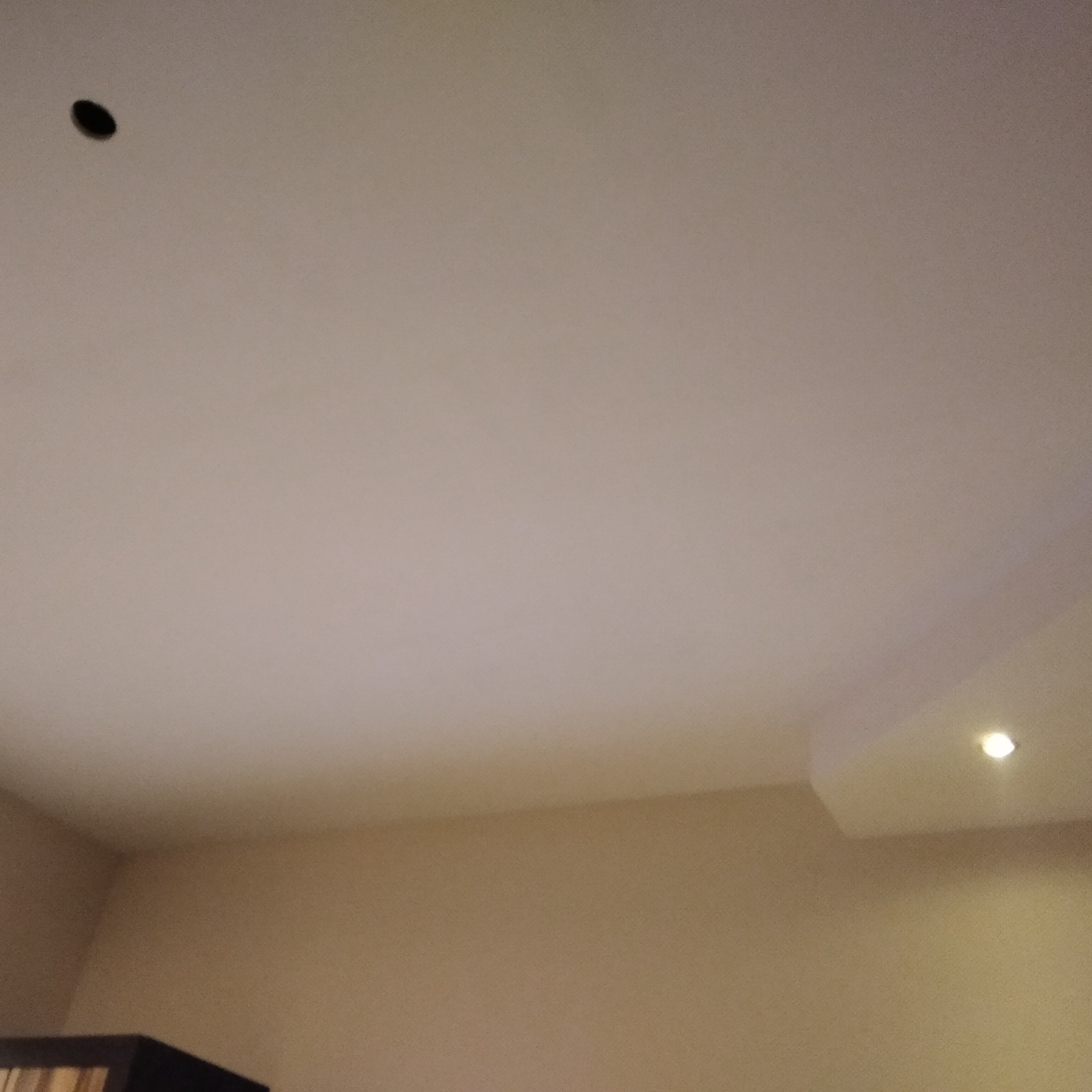 Pomieszczenie z pomalowanym sufitem na jasny kolor, widoczna instalacja oświetleniowa w rogu oraz ciemny otwór w suficie