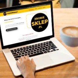 Osoba korzysta z laptopa, na ekranie widoczna strona internetowa 'ZrobieSklep.pl' z ofertą sklepów internetowych i marketingu, obok leży tablet i filiżanka cappuccino.