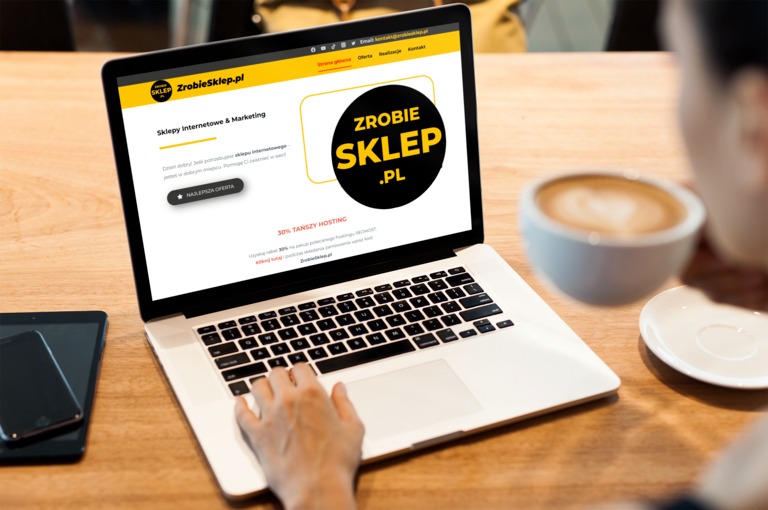 Osoba korzysta z laptopa, na ekranie widoczna strona internetowa 'ZrobieSklep.pl' z ofertą sklepów internetowych i marketingu, obok leży tablet i filiżanka cappuccino.