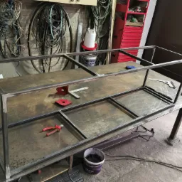 Konstrukcja z profili stalowych, wstępnie zespawana na stole warsztatowym, widoczne narzędzia: kątownik magnetyczny, szczypce, miarka, w tle ściana z kablami i półka z narzędziami.