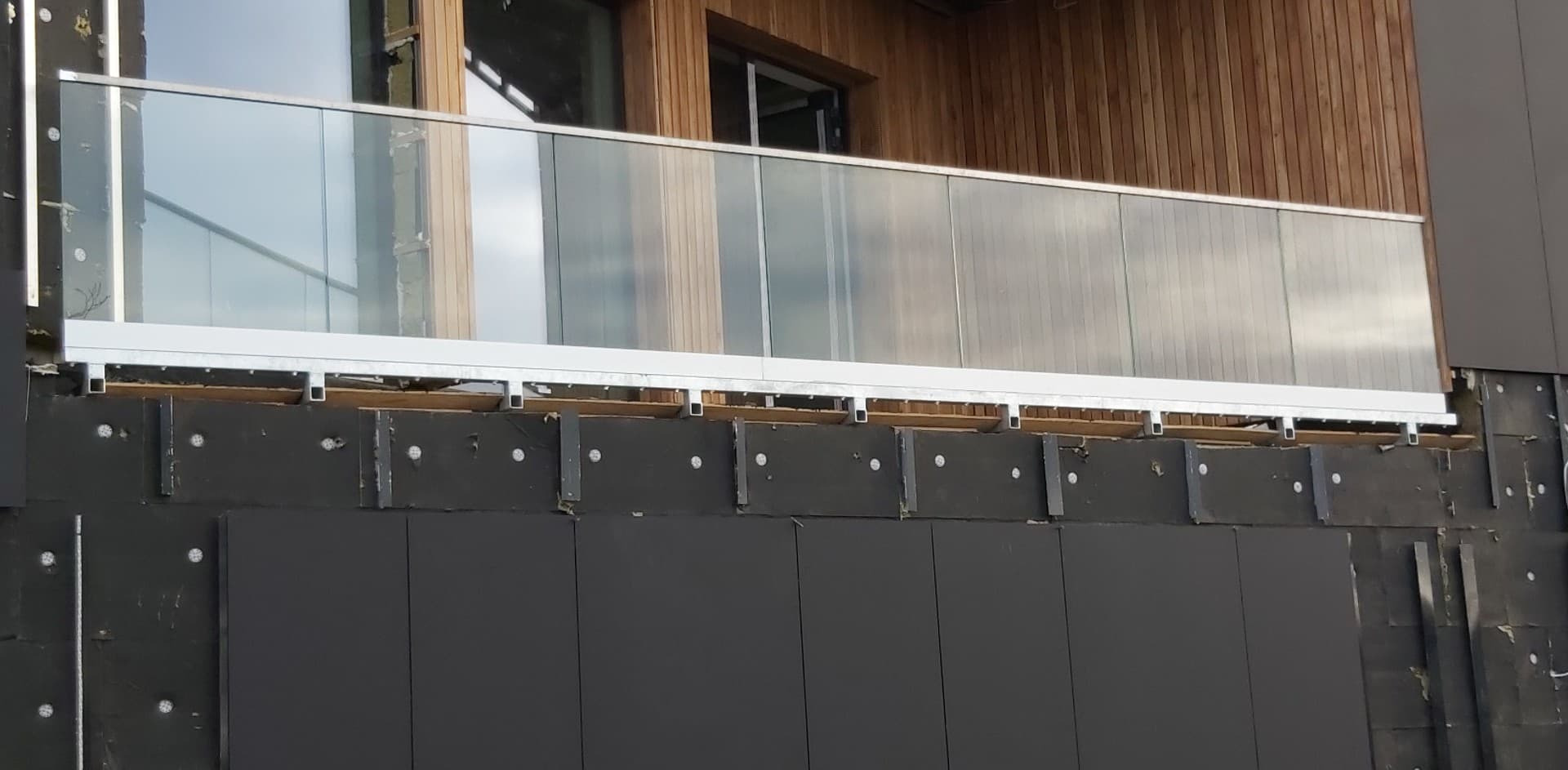 Montaż balustrady na balkonie z drewnianym wykończeniem, widoczne elementy konstrukcyjne i izolacja budynku.