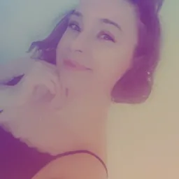 Portret młodej kobiety z upiętymi włosami, delikatnym uśmiechem i dłonią podpierającą brodę, sfotografowanej w miękkim, rozproszonym świetle.