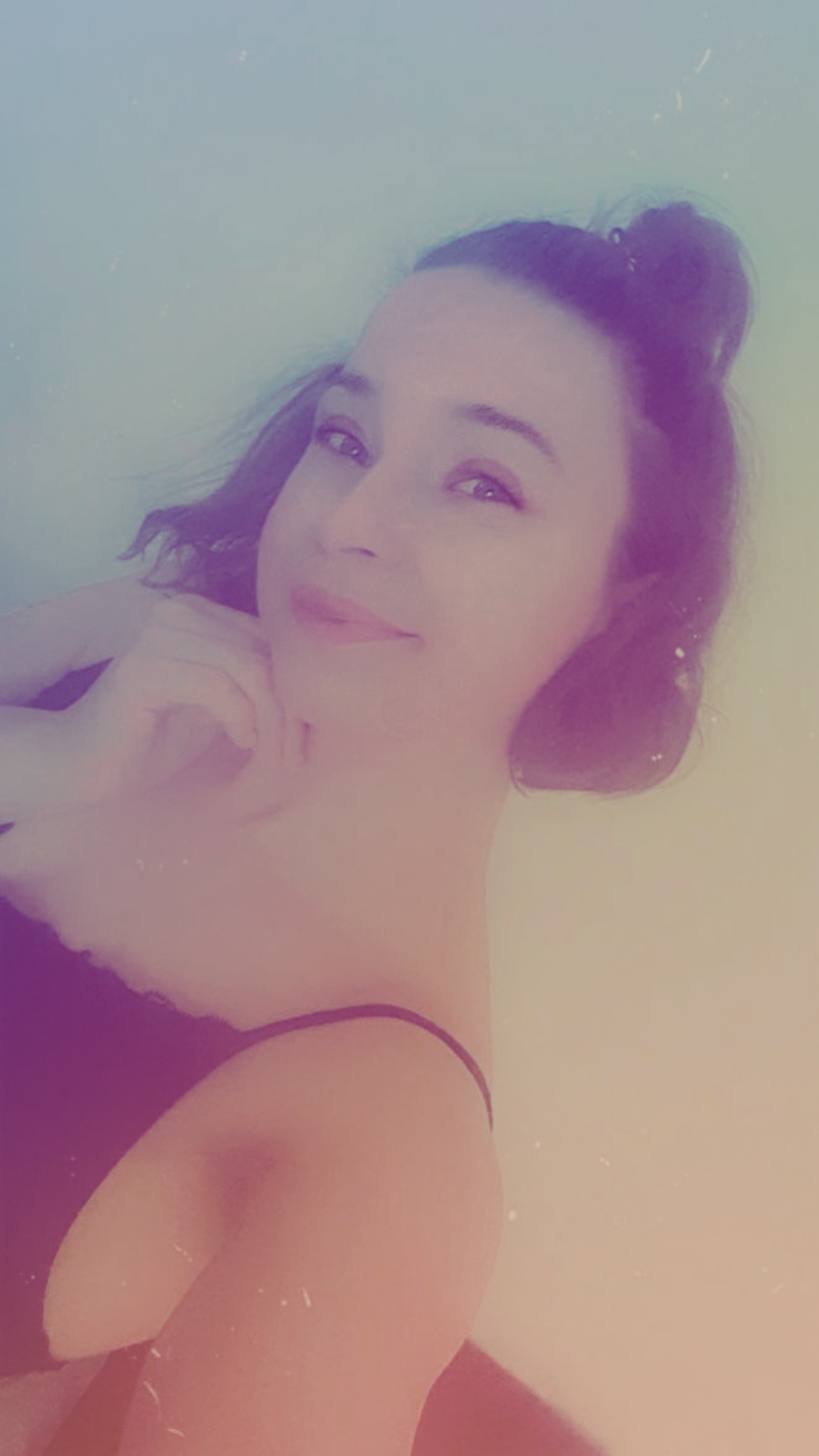 Portret młodej kobiety z upiętymi włosami, delikatnym uśmiechem i dłonią podpierającą brodę, sfotografowanej w miękkim, rozproszonym świetle.