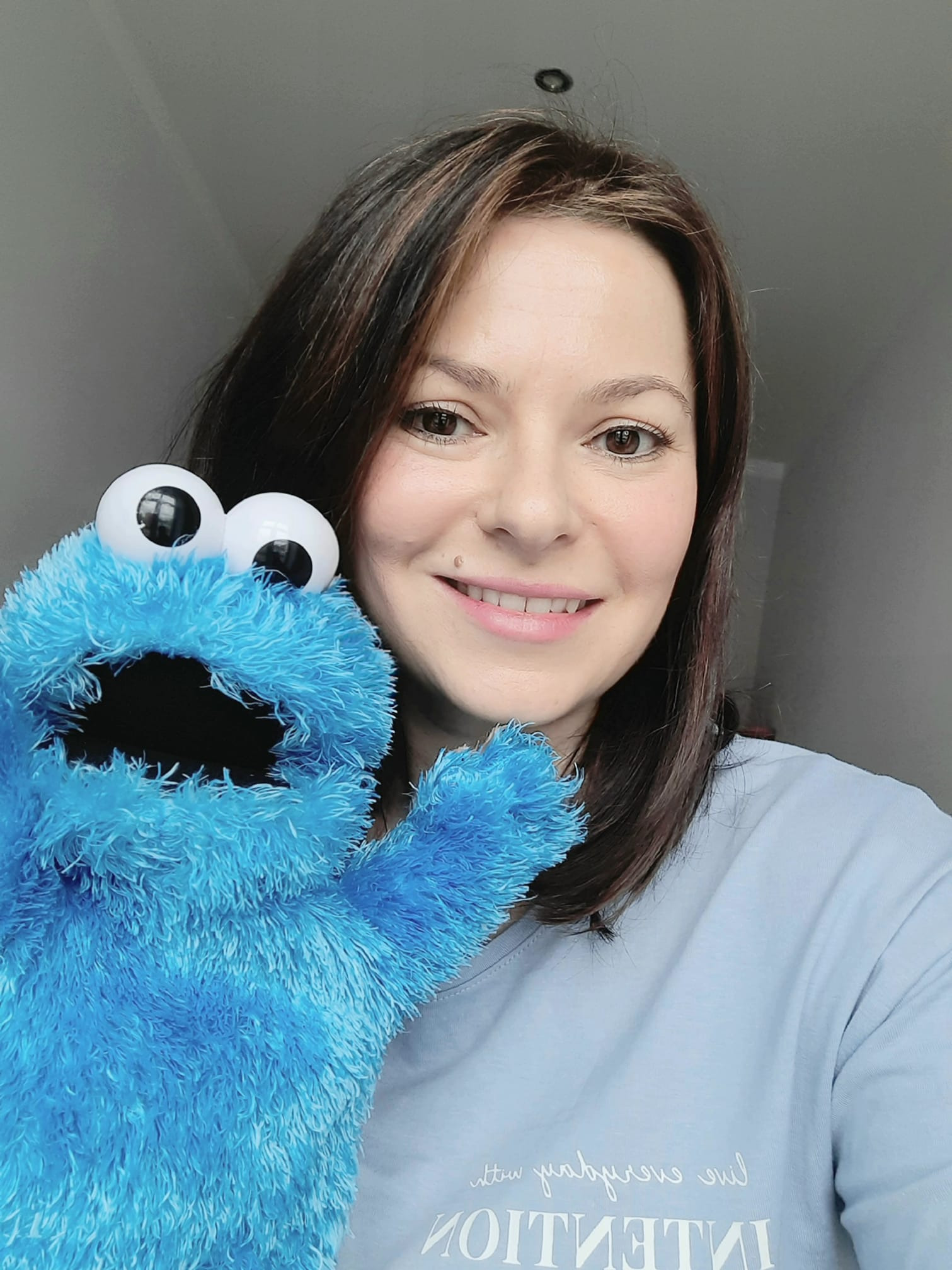 Uśmiechnięta kobieta z brązowymi włosami trzyma niebieską pacynkę z dużymi oczami, prawdopodobnie podczas sesji terapeutycznej lub zabawy.