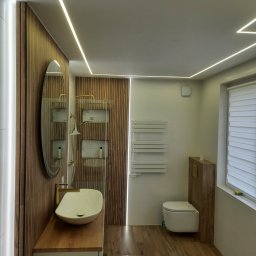 Usługi remontowo budowlane - Nowoczesna łazienka z drewnianymi akcentami, owalnym lustrem i podświetleniem LED. Umywalka nablatowa i drewnopodobne płytki podłogowe tworzą spójną całość.