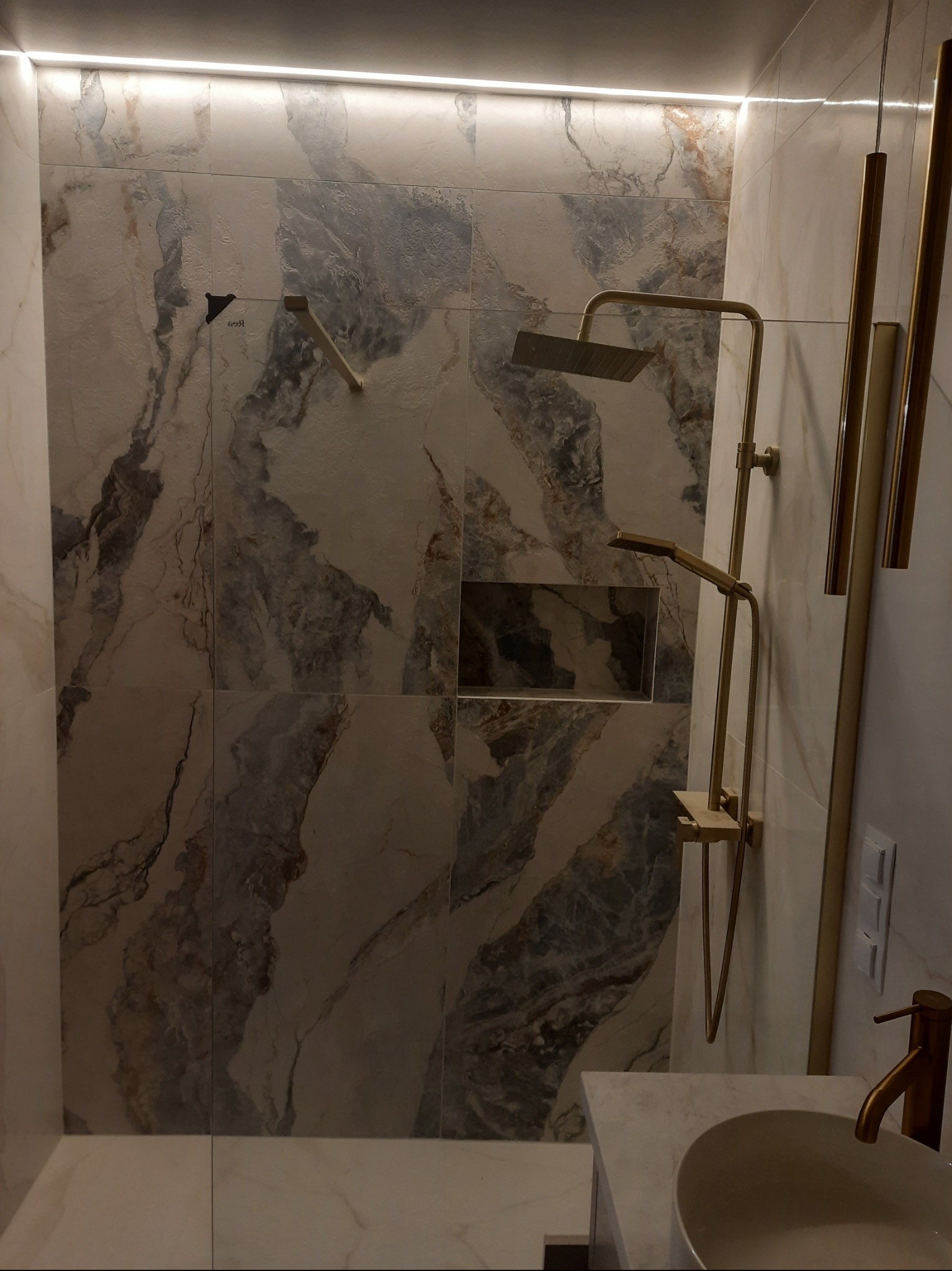 Wykończona łazienka z marmurowymi płytkami, złotą armaturą i oświetleniem LED. Nowoczesny design z dbałością o detale.