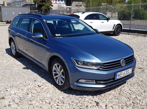 Niebieski Volkswagen Passat Variant na żwirowym parkingu, z widoczną tablicą rejestracyjną i białym SUV-em w tle.