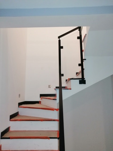 Schody wewnętrzne w trakcie montażu, zabezpieczone folią, z balustradą szklaną z czarnymi elementami mocującymi.