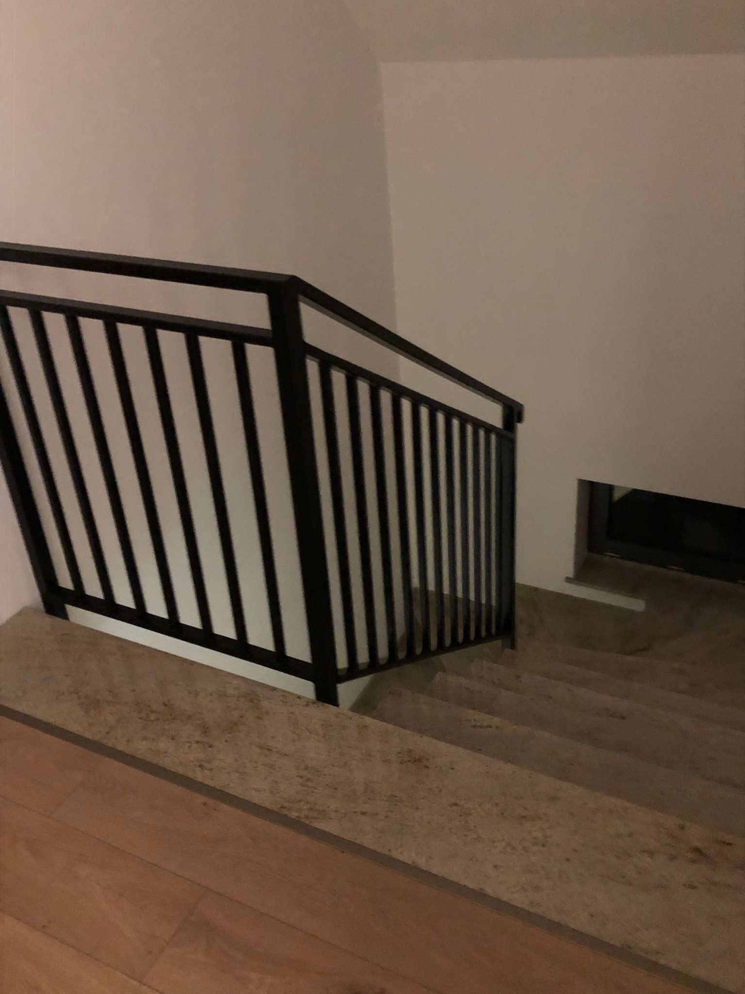 Wewnętrzne schody wykończone kamienną okładziną, zabezpieczone czarną, metalową balustradą z pionowymi szczeblami.