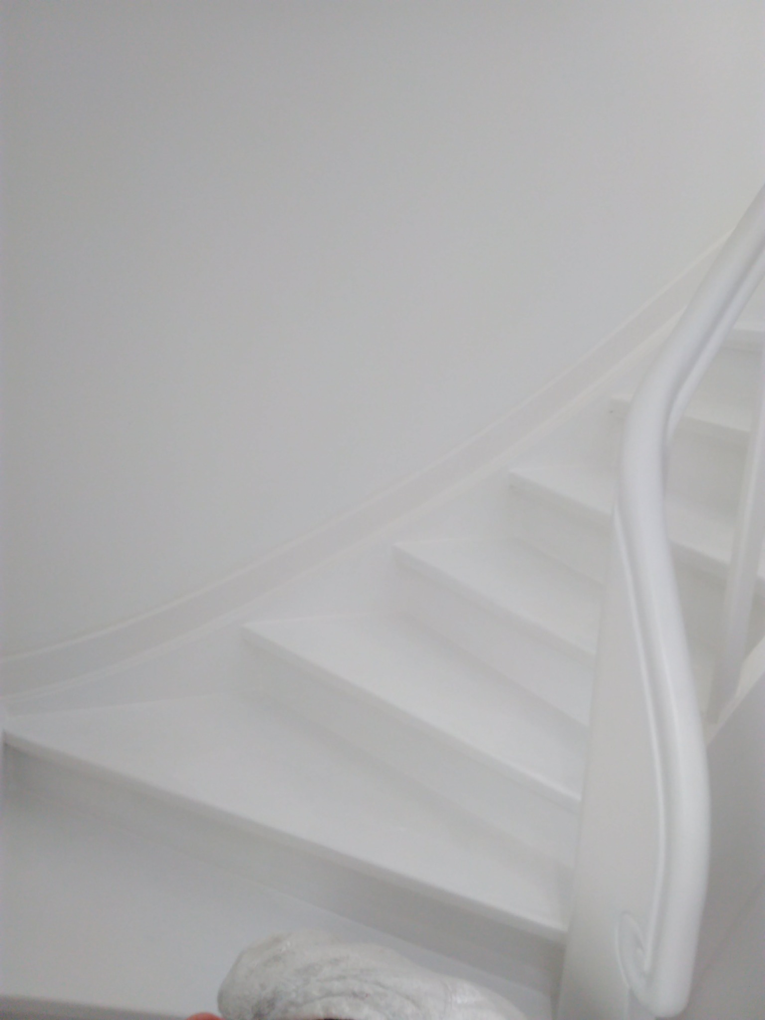 Białe, kręte schody z poręczą, świeżo pomalowane na biało, widok z dołu, z elementami zabezpieczającymi na dole.