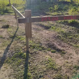 Wytyczony drewniany profil z czerwonymi oznaczeniami wysokościowymi na gruncie z trawą, służący do wyznaczania budynku.