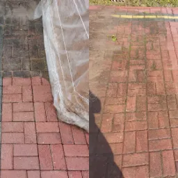 Częściowo wyczyszczona czerwona kostka brukowa, widoczny kontrast między brudną a czystą powierzchnią, zabezpieczona folią część kostki po lewej stronie, cień osoby w prawym dolnym rogu.