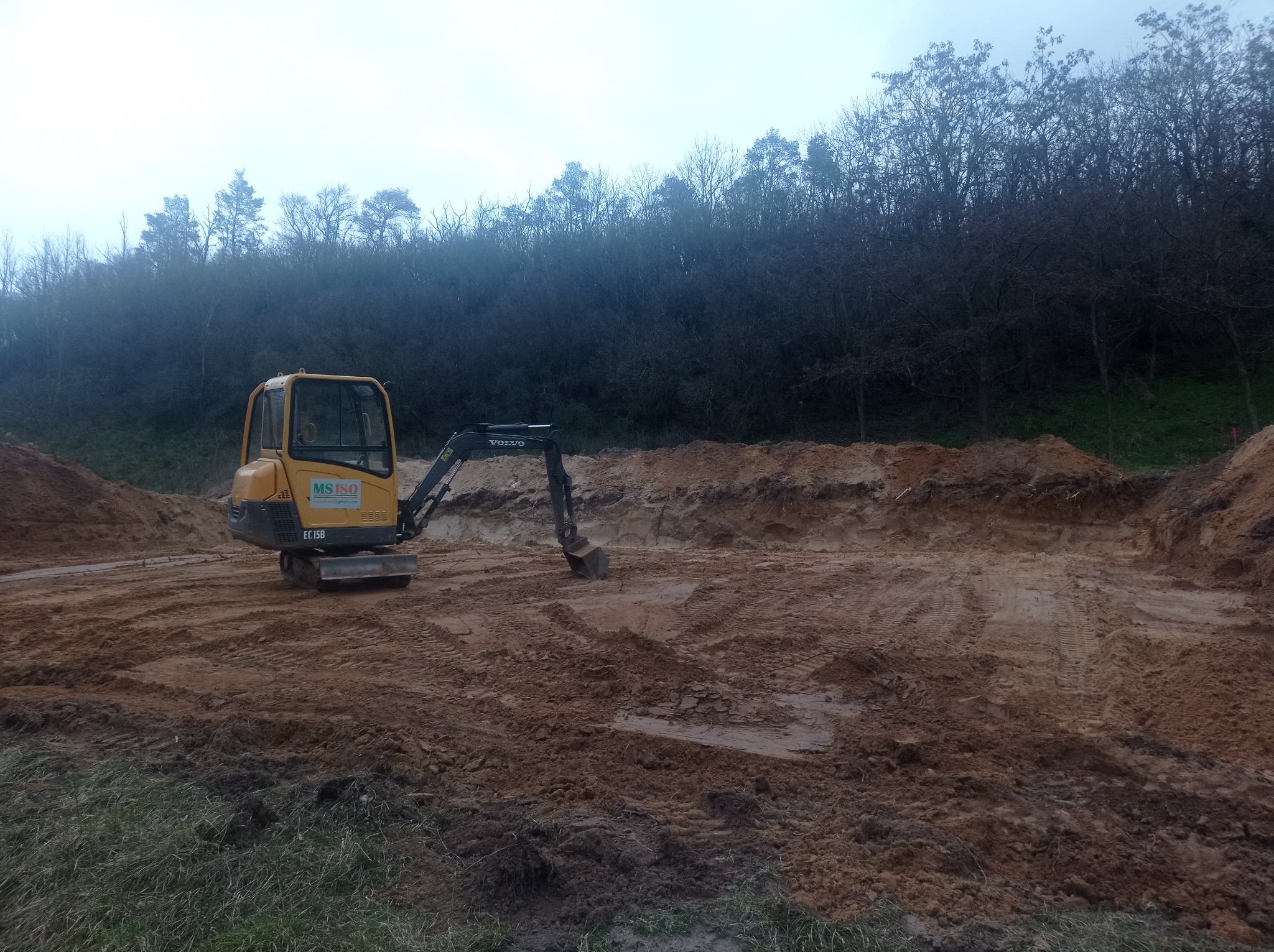 Żółta minikoparka Volvo EC15B na placu budowy, wykop pod staw w trakcie tworzenia, widoczne ślady opon na ziemi.
