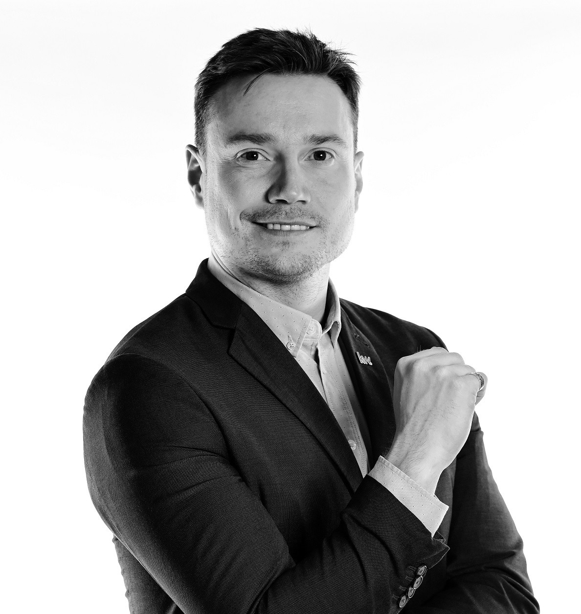 Portret uśmiechniętego mężczyzny w garniturze z Poznania, na białym tle, w czerni i bieli, z ręką zaciśniętą w pięść.