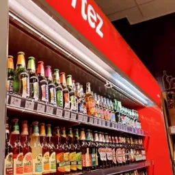 P&oacute;łki chłodnicze wypełnione r&oacute;żnorodnymi butelkami piwa i napoj&oacute;w alkoholowych, z widocznym logo 'Cortez' na czerwonym panelu nad nimi.