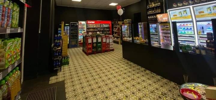 Wnętrze sklepu z napojami, widoczne regały chłodnicze z oświetleniem LED, palety z napojami w kartonach i ozdobna podłoga w geometryczne wzory.