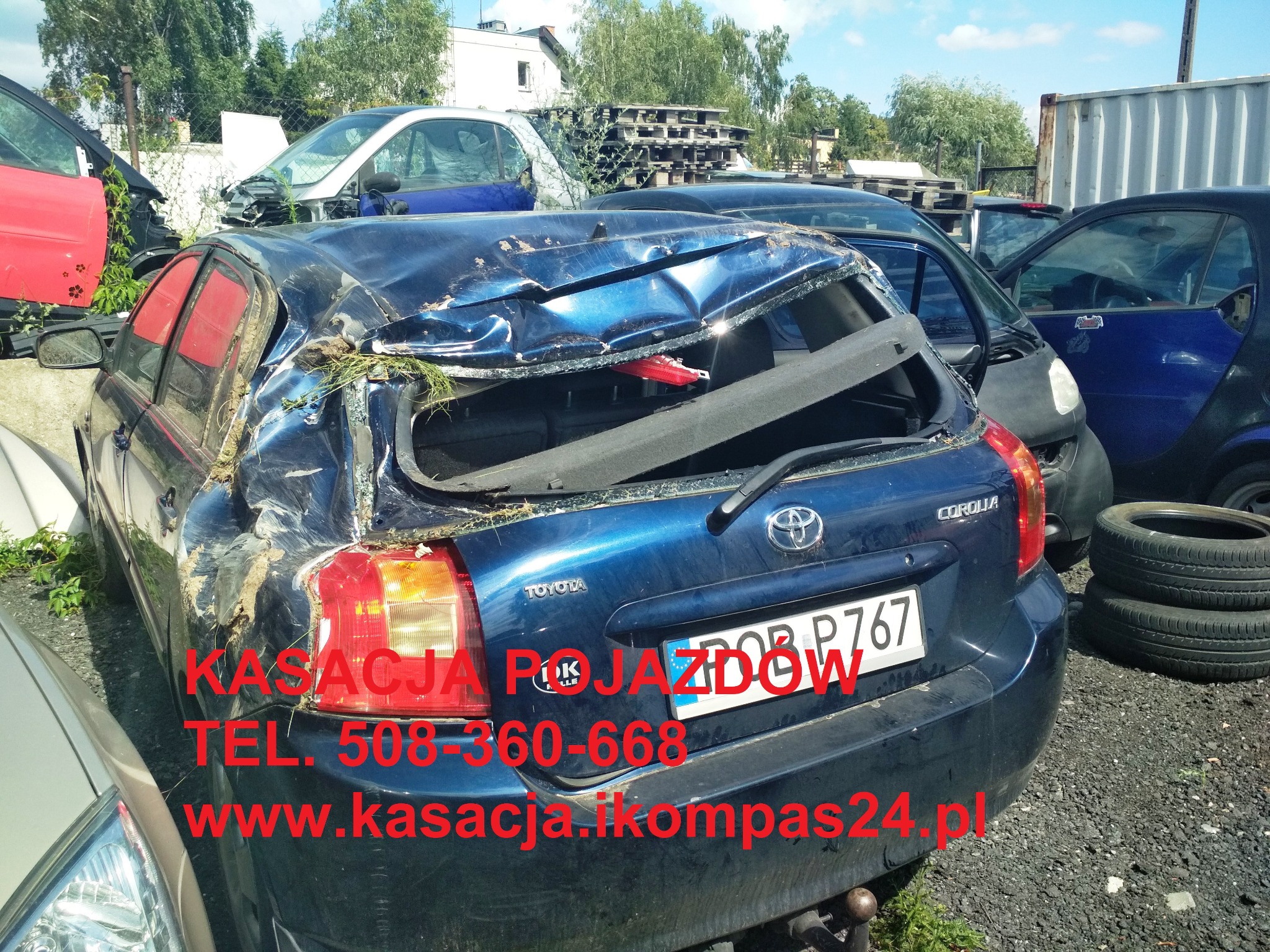Zniszczony, niebieski samochód Toyota Corolla z uszkodzonym tyłem, widoczne inne wraki aut w tle, na karoserii tekst reklamowy firmy zajmującej się kasacją pojazdów.