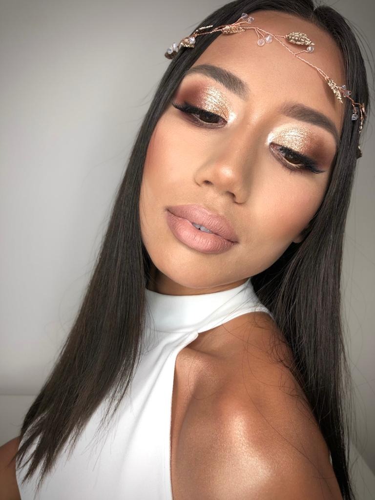 Portret kobiety z wyrazistym, złotym cieniowaniem powiek i delikatnym różem na policzkach, uzupełnionym przez ozdobną opaskę na włosach z koralikami.