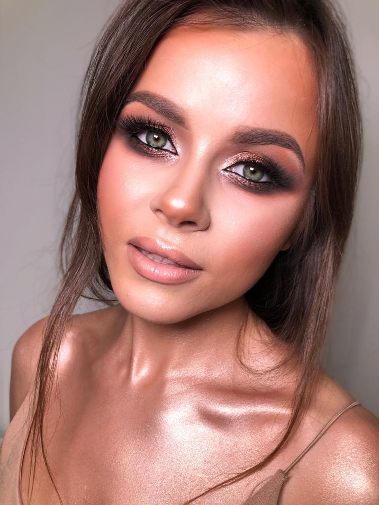 Portret kobiety z wieczorowym upiększeniem oczu w odcieniach brązu i czerni, rozświetlona cera i usta w naturalnym kolorze, widoczne brwi podkreślone i sztuczne rzęsy.