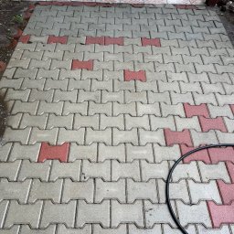 CDM COMPANY SP. Z O.O. - Umyta kostka brukowa w odcieniach szarości i czerwieni, z fragmentem czarnego węża ogrodowego w prawym dolnym rogu. Widoczne ślady wilgoci po czyszczeniu.