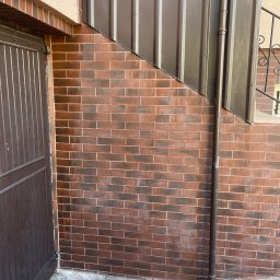 CDM COMPANY SP. Z O.O. - Ceglana elewacja budynku po czyszczeniu, z widoczną rynną i fragmentem metalowego dachu. Czysta powierzchnia, brązowe odcienie cegieł i metalu.