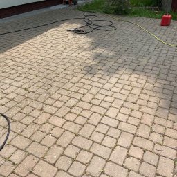 CDM COMPANY SP. Z O.O. - Kostka brukowa z chwastami, przygotowana do czyszczenia. W tle myjka ciśnieniowa i kanister. Widok z góry, oświetlenie słoneczne.
