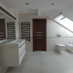 Nowoczesna łazienka na poddaszu z beżowymi płytkami, białymi sanitariatami i grzejnikiem drabinkowym.