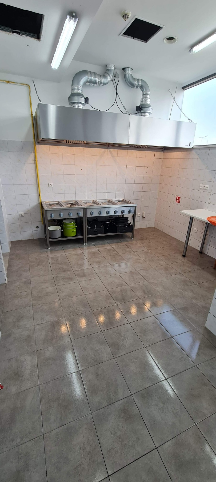 Wnętrze kuchni przemysłowej z profesjonalnym piecem gazowym, okapem i wyłożonymi kafelkami ścianami oraz podłogą, widok z perspektywy podłogi.