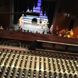 Konsoleta mikserska z widokiem na scenę teatralną podczas występu z publicznością w tle.