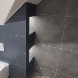 ANATOLII - Wykończona łazienka na poddaszu z szarymi płytkami ściennymi, drewnopodobną podłogą i wnęką z podświetleniem LED, widoczny odpływ liniowy.