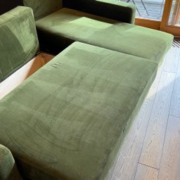 Górska Opieka Nieruchomości Paweł Strzępek - Rozłożysta sofa w odcieniach zieleni na drewnianej podłodze, z widokiem na balkon przez okno. Minimalistyczny design i naturalne materiały.